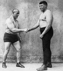 Black-and-white photograph of two men shaking hands in front of a grey wall