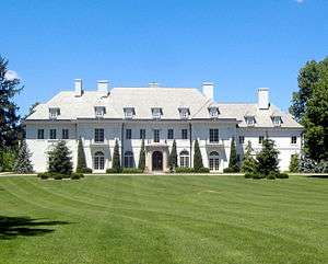 White mansion with four chimneys, trees lining the front, and many windows