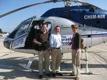 Two men on the left and a woman on the right flanking the open door of a helicopter.