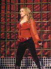 A blonde woman wearing a red shirt and dark pants is performing