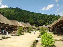 Street lined by similar wooden houses with white walls and thatched roofs.