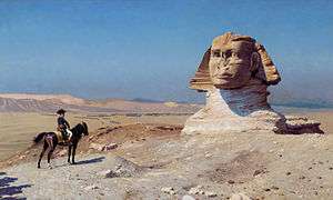 Small figure on a horse looks towards a giant statue in the desert, with a blue sky