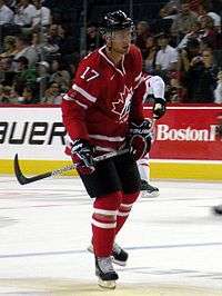 Hockey player in red uniform. He holds his stick as if preparing to hit the puck.