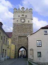  View of a street of old buildings, the largest of which is a tall clock tower with an archway