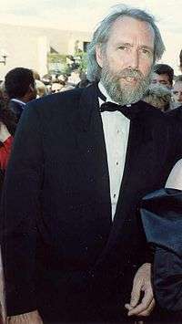 A tall, thin man in his early fifties, with salty-gray hair and a full beard, and wearing a tuxedo.