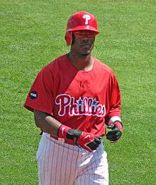 A man in a red baseball uniform and wearing a red helmet looks straight ahead