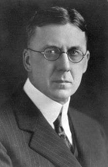 A severe-looking man in round-rimmed glasses