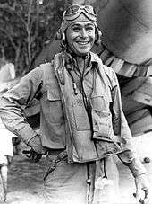 A young-looking man in pilot gear standing in front of a group of trees.