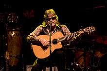 A man is sitting on a stool playing a guitar.