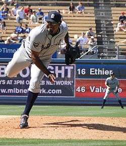 A man with a gray uniform and navy blue hat throws a pitch.