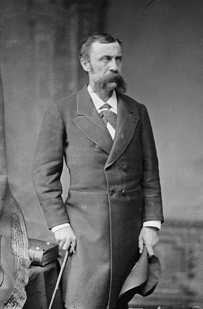 A man with a large moustache, dressed in a 19th century suit.