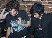 Two men, dressed in black, at a mixing table in a brick room