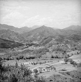 A series of ridgelines and steep hills in the distance, with light to medium vegetation. In the foreground is an open valley.