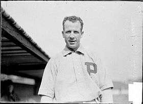 A smiling dark-haired man in a white baseball jersey with a block "P" over the left breast