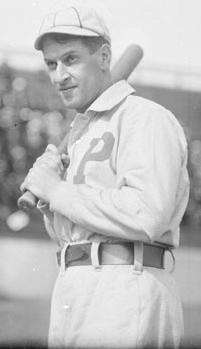 A black-and-white photograph of a man in a white baseball uniform with the letter "P" over the left side of his chest holding a baseball bat over his right shoulder.