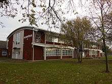 A two-story modern building of red brick and white-painted metal with glass windows and a curved white roof, with "King George V College" visible on one side.