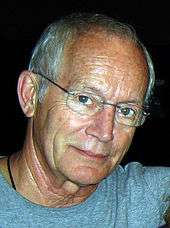 A man with white hair, wearing glasses