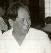 A smiling middle-aged man wearing a V-necked white collarless shirt