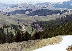 Photograph of the view from Lemhi Pass, eastward over the rolling, green, and partially wooded Bitterroot Mountains.