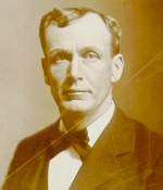 Sepia tone image of the head and shoulders of a clean-shaven middle-aged man in a suit and tie