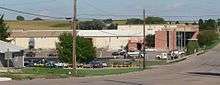 Large one-story brick and sheet-metal building, with large parking lot in foreground