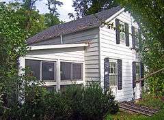 A white house with black shutters seen very close, with shrubs at the edge of the frame