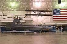 Starboard view of jet aircraft in museum among suspended aircraft and an American flag.