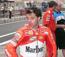 A man in red leathers at a race track, with two people in the background.