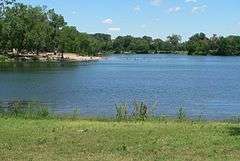 Small lake seen from grassy bank; swimming beach in distance