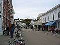 alt=The downtown of a small town, showing many buildings, some pedestrians and a horse-drawn wagon.