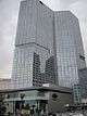 Ground level view of a 47-story building with a rectangular cross section and an all-glass facade; the building is still under construction, and a crane is visible on its roof.