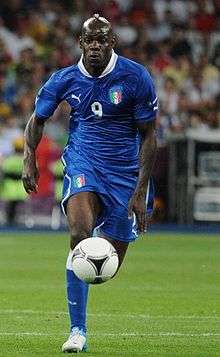 Full-body colour photograph of Mario Balotelli playing football during a match in 2012.