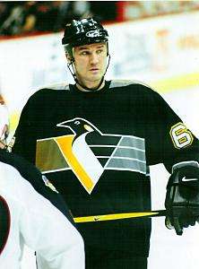 Hockey player in dark uniform. He holds his stick with both hands and looks onward, head tilted slightly.