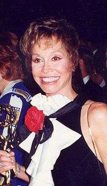 A smiling women wearing a black and white dress holds a golden statuette.