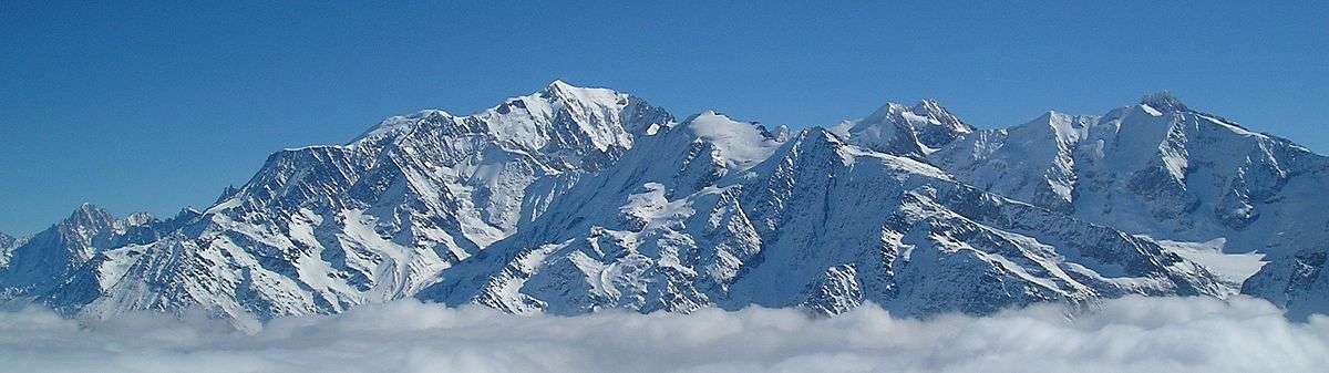 panorama of Mont Blanc mountain range above gray clouds under a blue sky