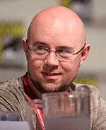 A black and white photograph of a man with a small beard and a bald head, wearing glasses.