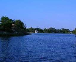 Still blue water surrounded by green trees and houses.