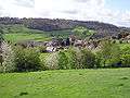 The roofs of houses and farm buildings in a green valley. Trees in the foreground