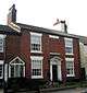 A brick house with four sash windows and one window bricked up.