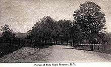 A highway flanked on both sides by fence and trees proceeds through mostly open land.