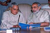 Modi and former Prime Minister Vajpayee looking at a blue-covered report