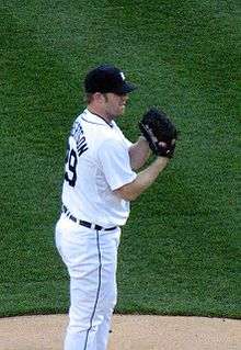 A man wearing a white baseball uniform and a dark baseball cap