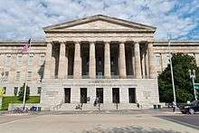 A 3 story building. The first story is granite, while the second two are sandstone. There is a pedimented front with columns spanning the second and third floors and the entrance on the first.