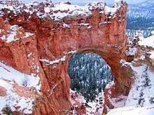 A large opening in red rock with snow on top