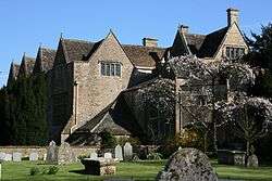 Old mansion house with triangular roofs. In the foreground is a garden with gravestones.