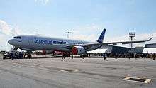 A A330-200F in Airbus's white and blue livery on display under a partly cloudy but otherwise clear sky. The engine inlets are covered.