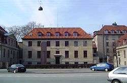 A block shaped beige building with a sloped, red tiled roof