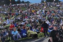 A crowd of people sitting on grass and in folding chairs