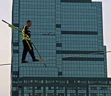 A man tightrop walks with a large building in the background