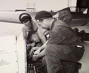 Three men in overalls working on an aircraft engine